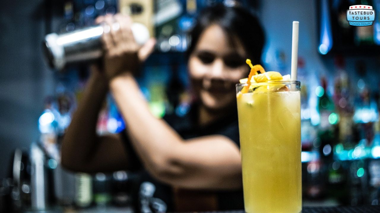 Bartender shaking a cocktail shaker with a yellow drink in the foreground.