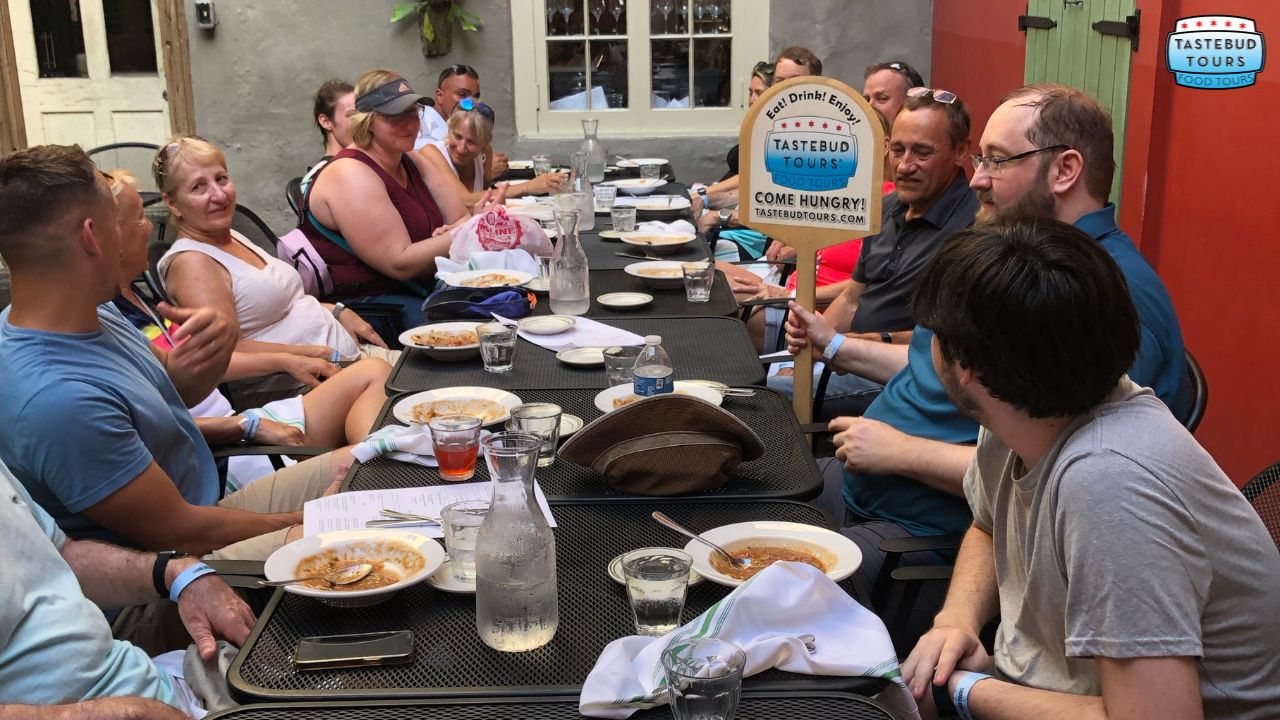 culinary-tours-for-food-enthusiasts Group of people dining outdoors, engaged in conversation, with 'Tastebud Tours' signs visible.