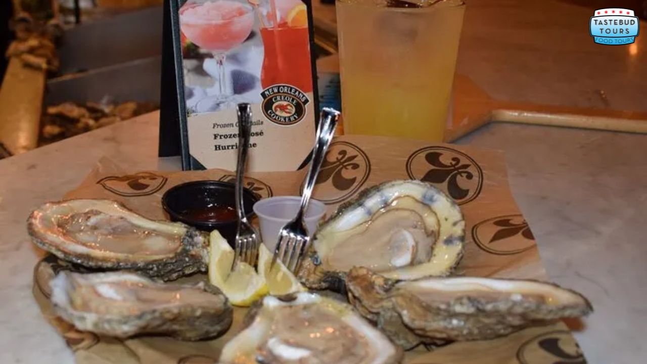 Plate of raw oysters with lemon wedges, sauces, and beverages on a table.