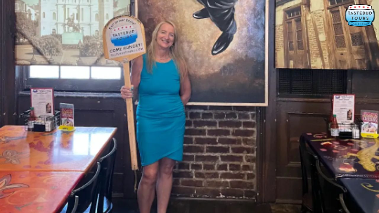 Woman in blue dress holding a Tastebud Tours sign in a restaurant with art on the walls.