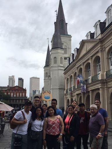 Group of people posing in front of a historic building with spires on a cloudy day.