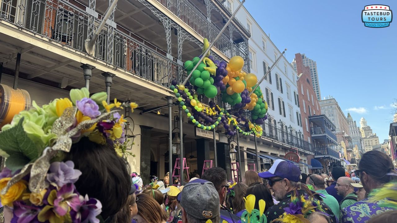 Crowd in colorful attire at festive street with balloons and decorated balconies.