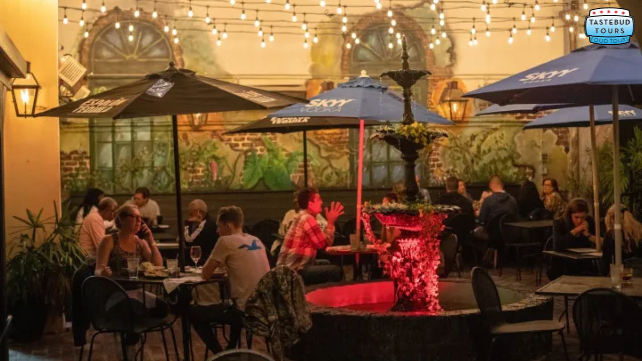 Outdoor restaurant with string lights, umbrellas, and a central fountain surrounded by diners.