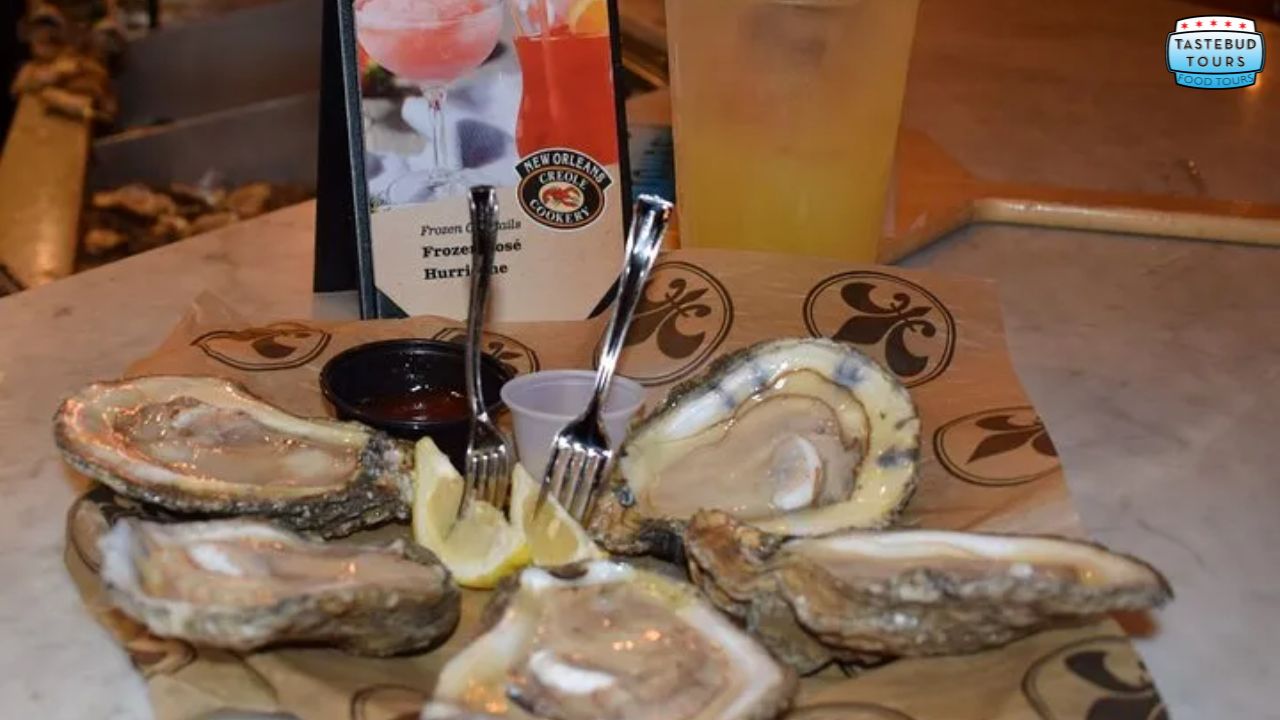 Plate of oysters with lemon wedges and forks, accompanied by a drink and a menu on the side.