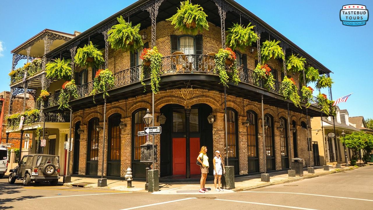 Historic building with balcony and plants at street corner with two people standing outside.