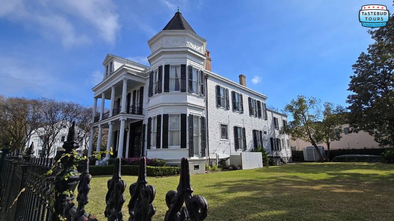 Elegant white Victorian house with black shutters and a turret on a sunny day.