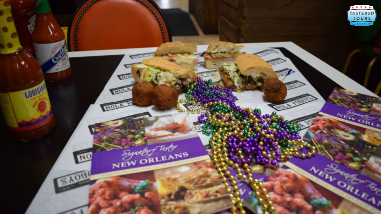 Sandwiches, Mardi Gras beads, and tour brochures on a table with hot sauce bottles.