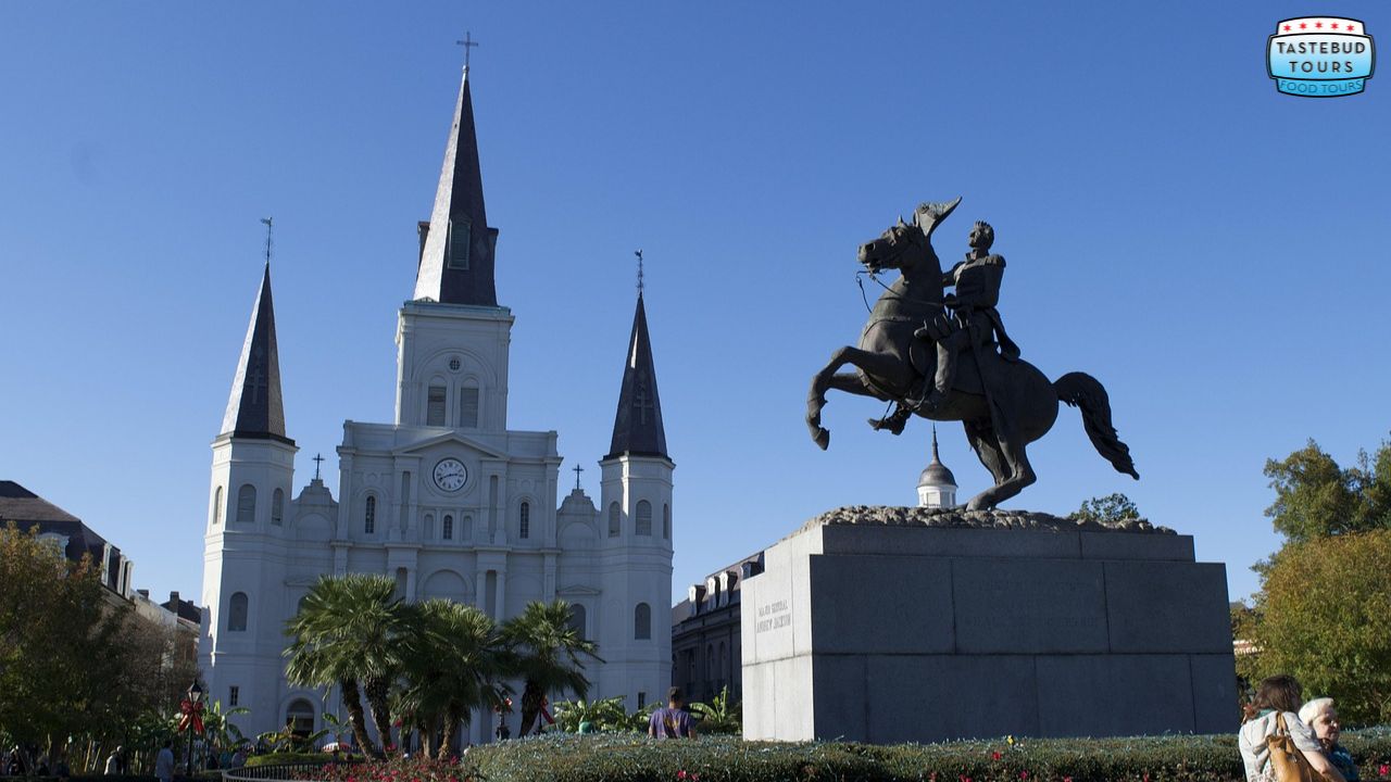 Statue of a rider and horse near a cathedral with three spires under a clear blue sky.