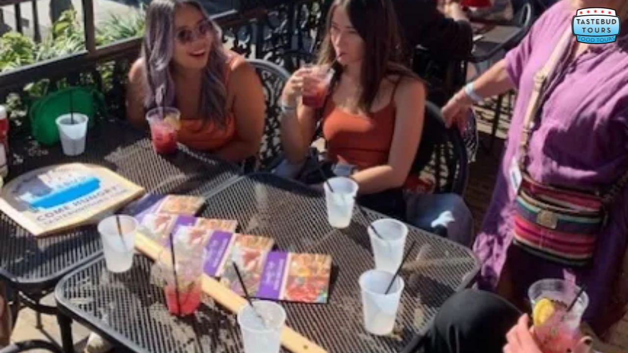 People sitting at an outdoor table with drinks and smiling, under sunlight.