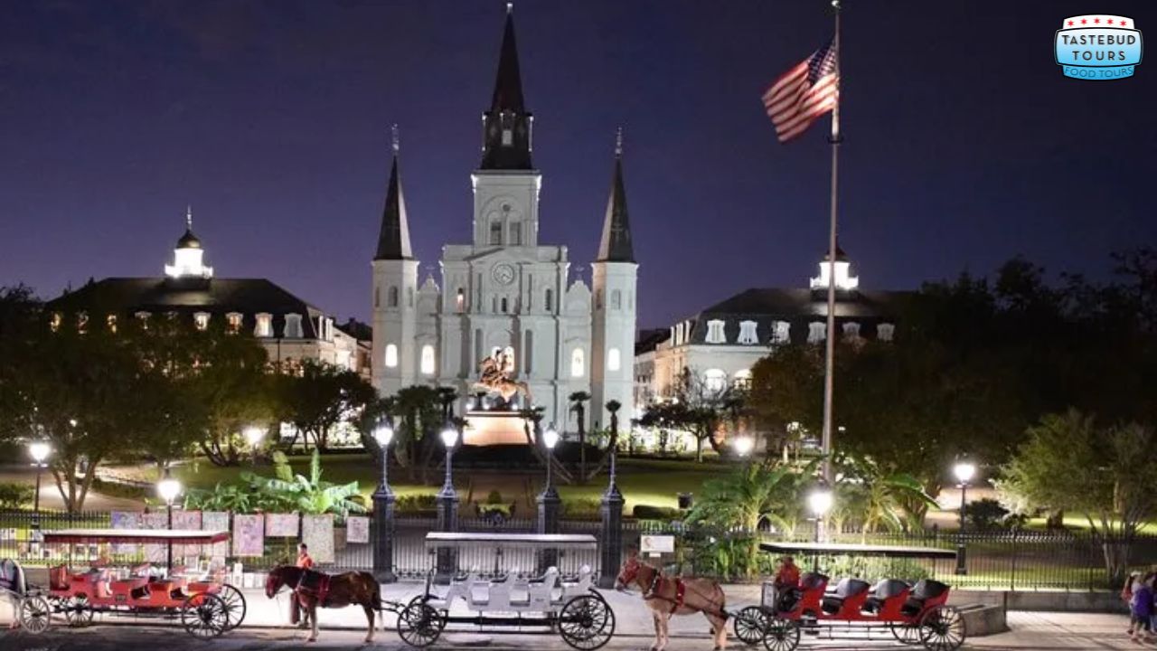 Night view of a lit cathedral with horse-drawn carriages and a U.S. flag in the foreground.