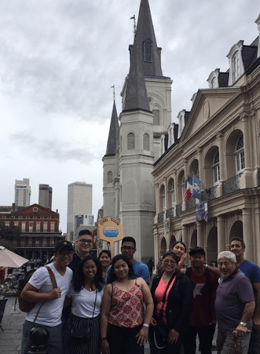 Group standing in front of a historic church with a tall spire on a cloudy day.
