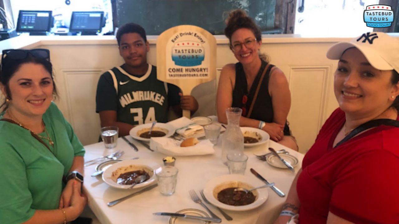 Four people dining at a table with bowls of food and a 'Tastebud Tours' sign.