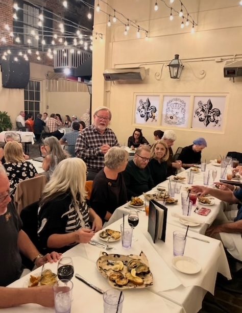 A group of people dining at a long table under string lights in a restaurant.