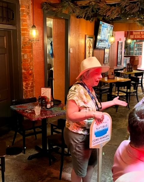 Person with hat and sign talks in restaurant with brick walls and TV in background.