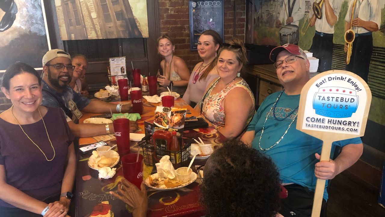 Group of people at a restaurant table with a food tour sign.
