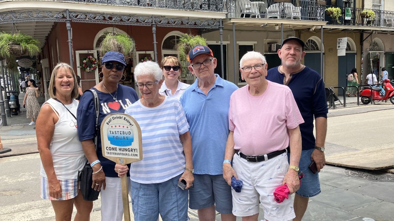 Group of people posing with a Tastebud Tours sign on a city street.