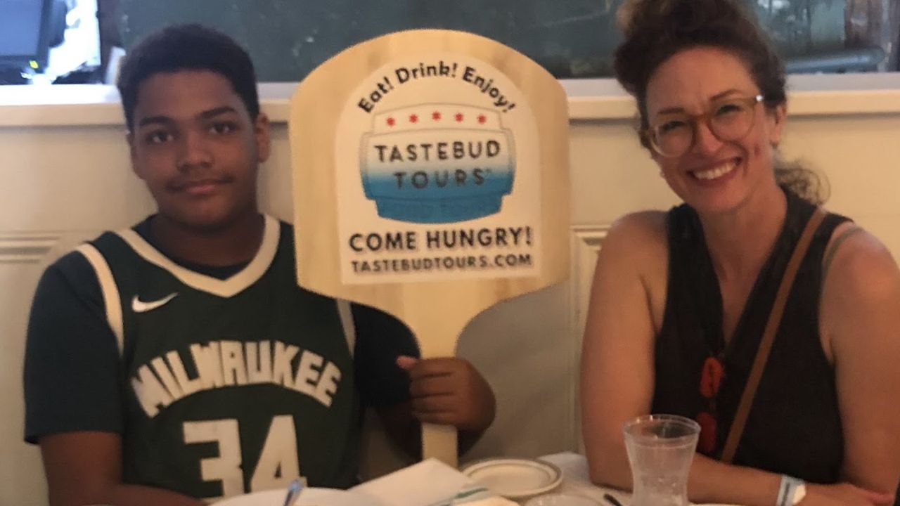 Two people sit at a table with a Tastebud Tours sign between them.