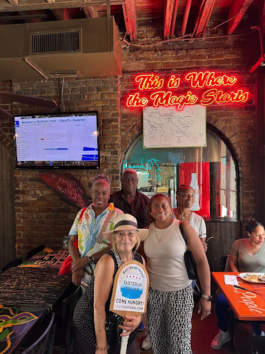 Group of people posing inside a restaurant with a neon sign and a TV on the wall.