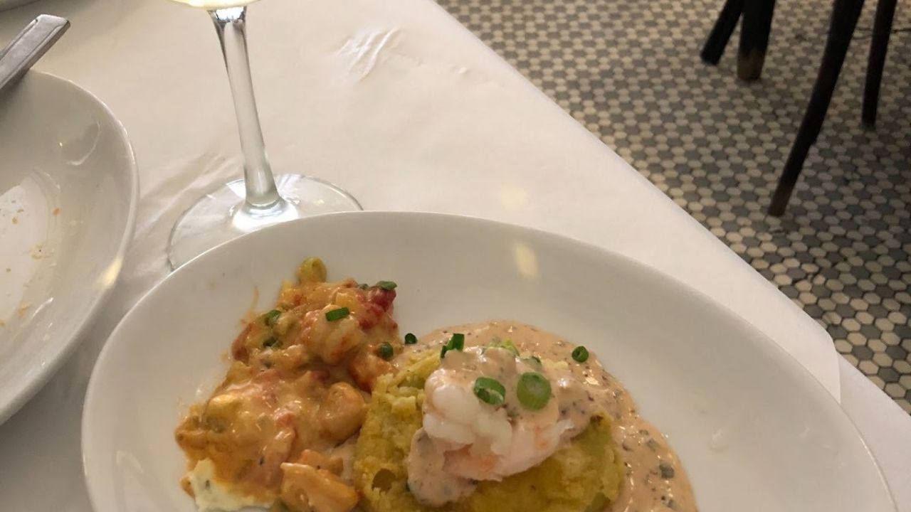 A plated dish with seafood and sauce served on a white plate next to a glass of white wine in New Orleans.