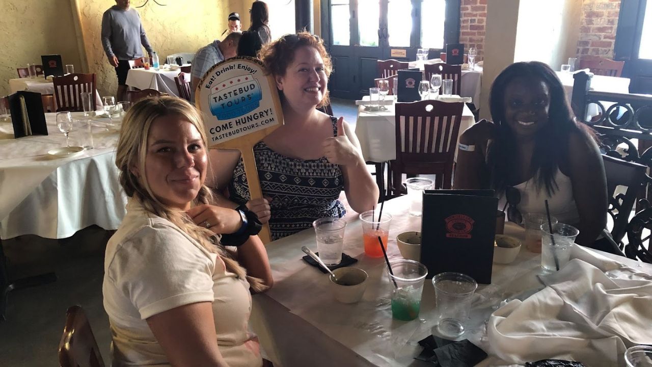 Team brunch group seated at a restaurant table, smiling and holding a Tastebud Tours sign.