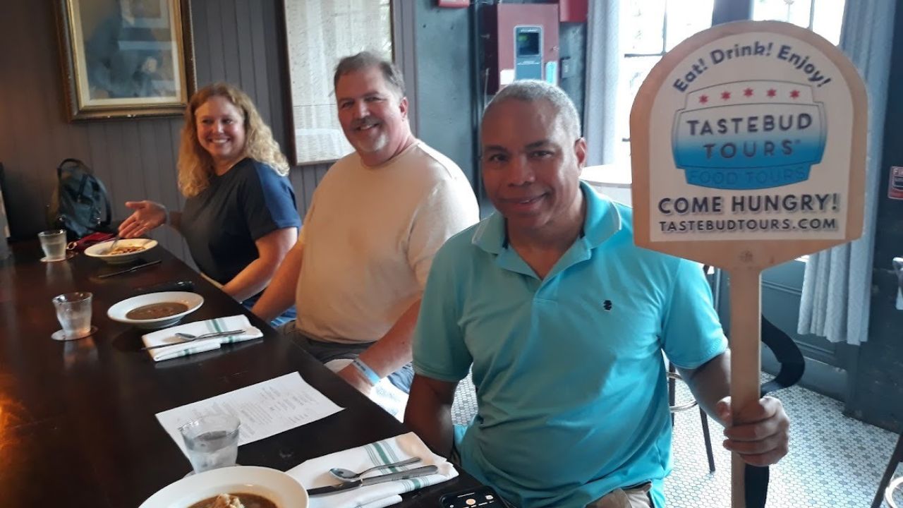Team brunch trio enjoying a cozy restaurant meal, smiling beside a Tastebud Tours sign.