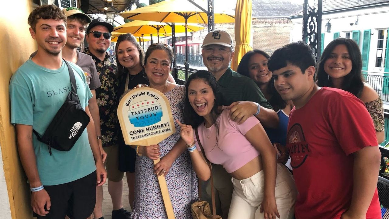 Team brunch group smiling together on a balcony, holding a Tastebud Tours sign.