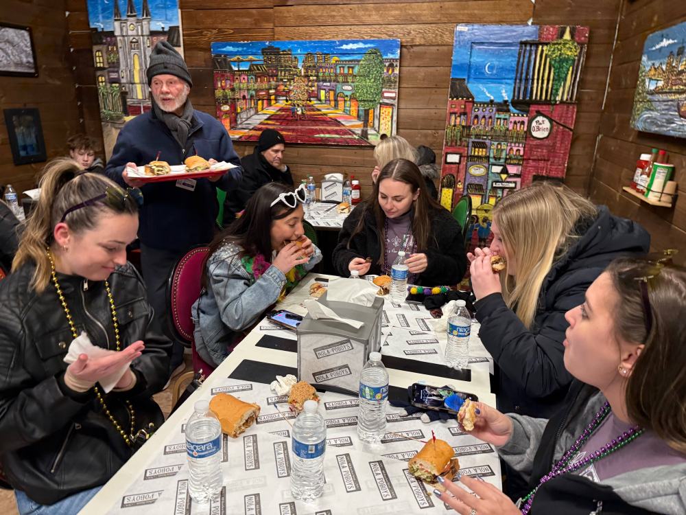 Tourists trying crispy po’boy sandwich filled with seafood and fresh ingredients.