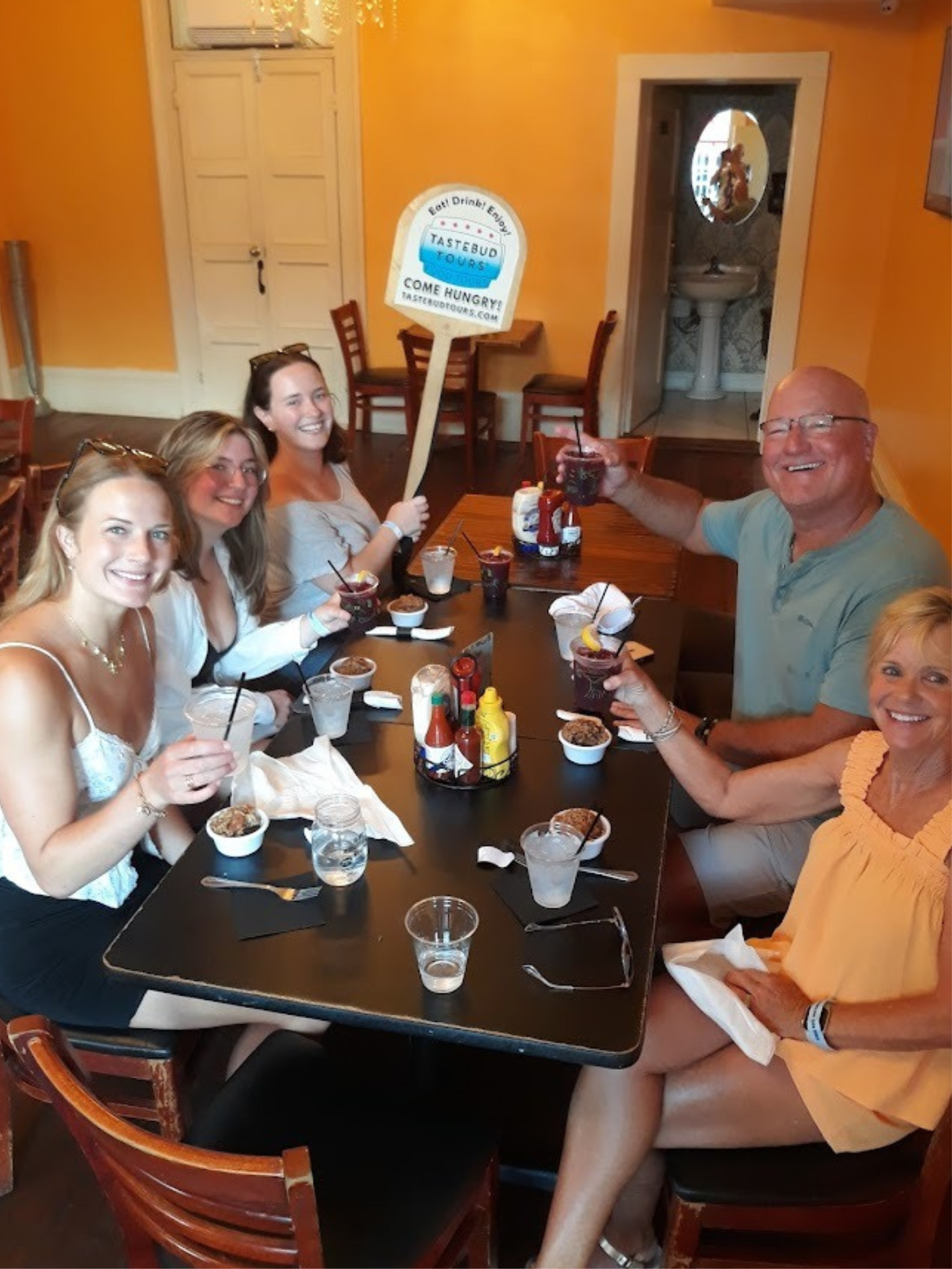 Group of five people smiling at a restaurant table with drinks.