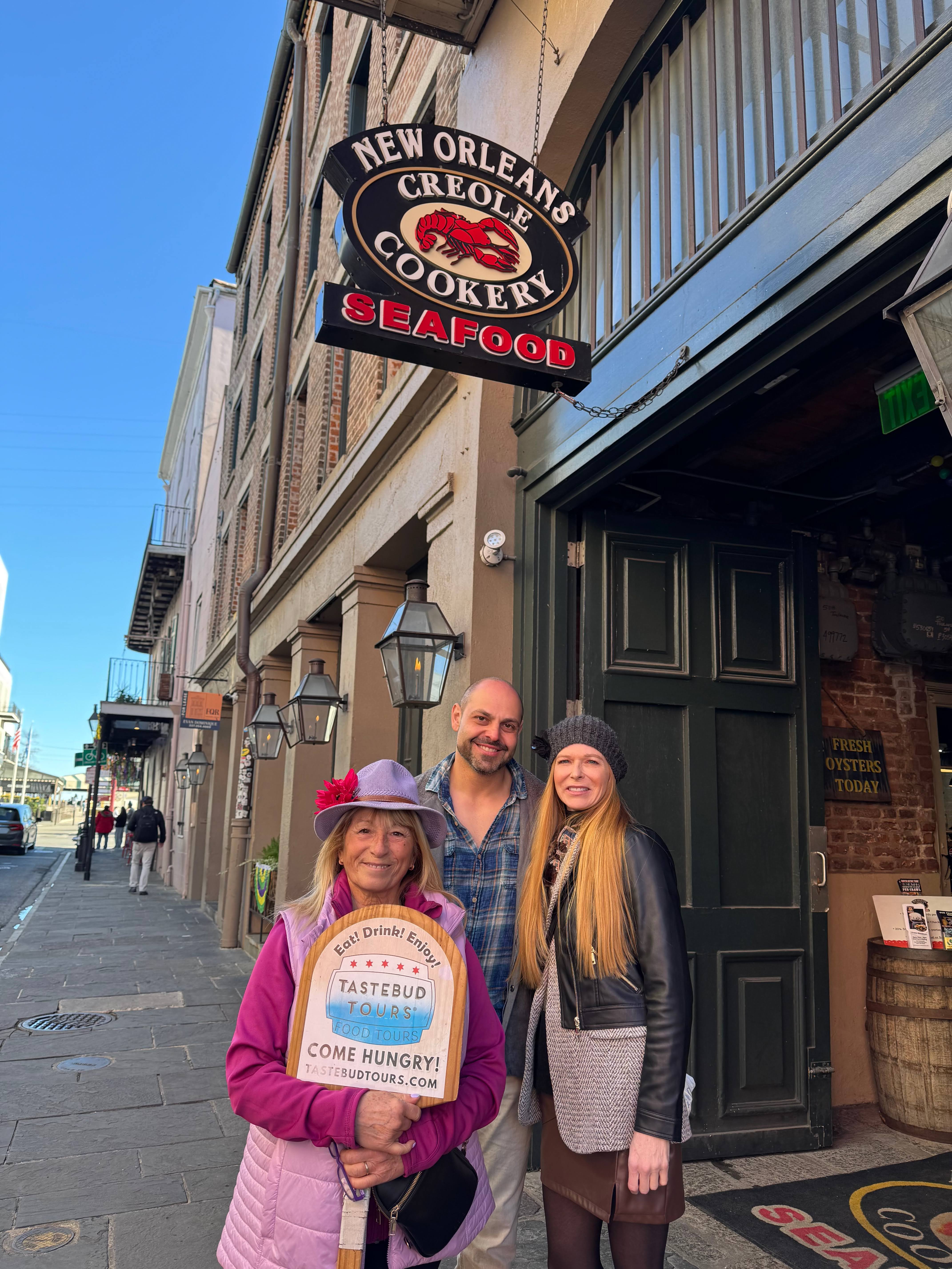 Guests standing outside a New Orleans Creole Cookery holding a Tastebud Tours sign.