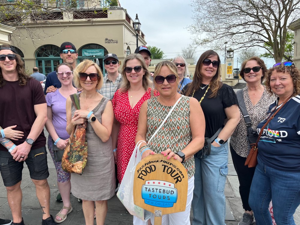 Tastebud Tours group posing with a food tour sign in New Orleans.
