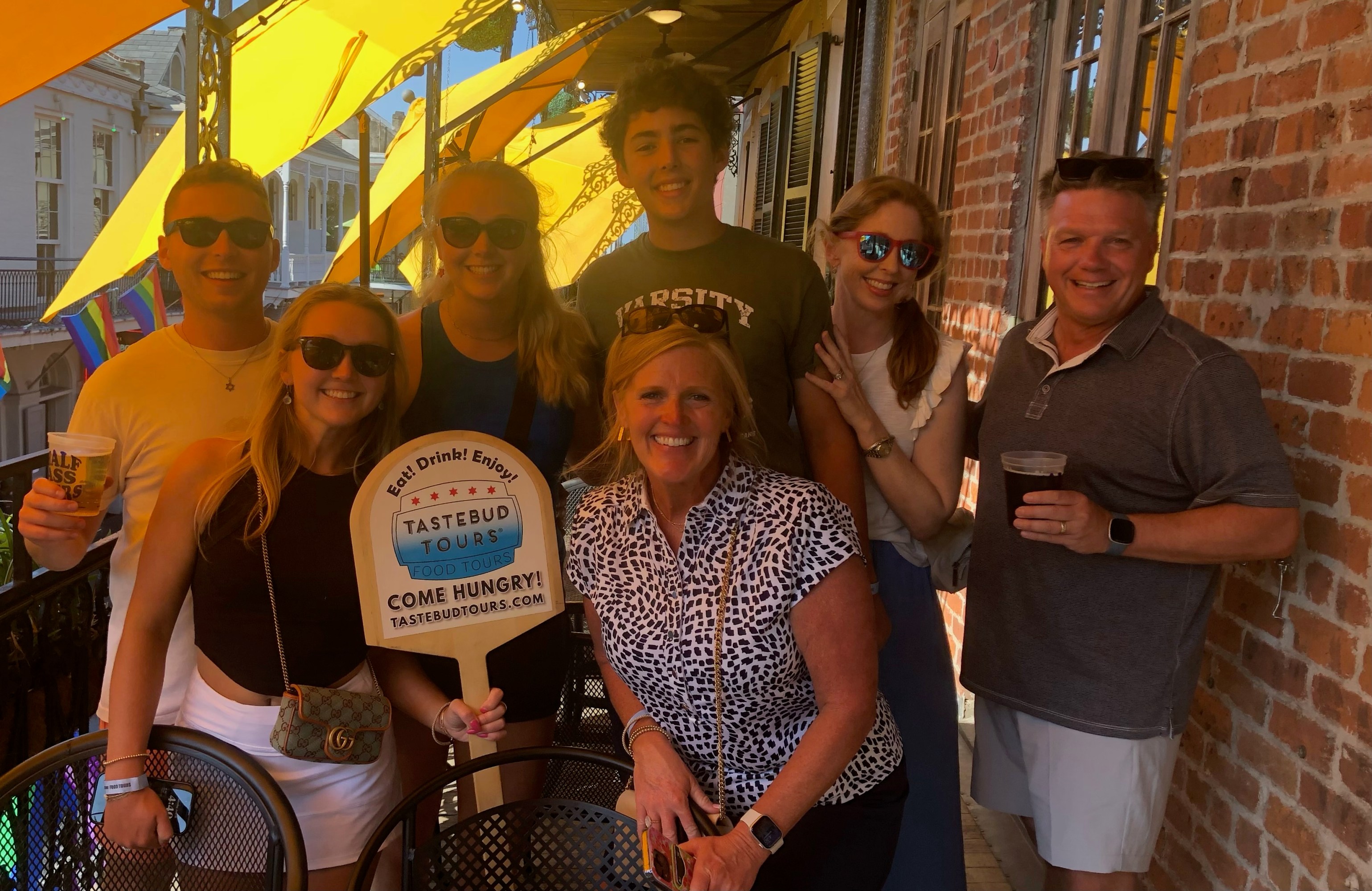 Group of seven Tastebud Tours guests smiling on a French Quarter balcony in New Orleans.