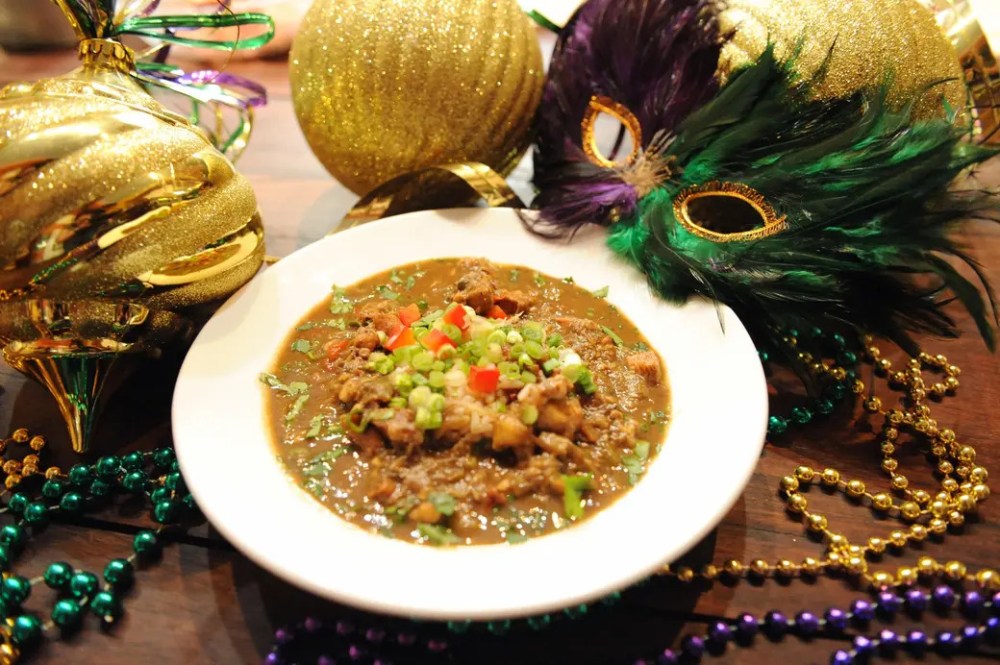 Mardi Gras food featuring a bowl of gumbo surrounded by colorful beads and festive masks.