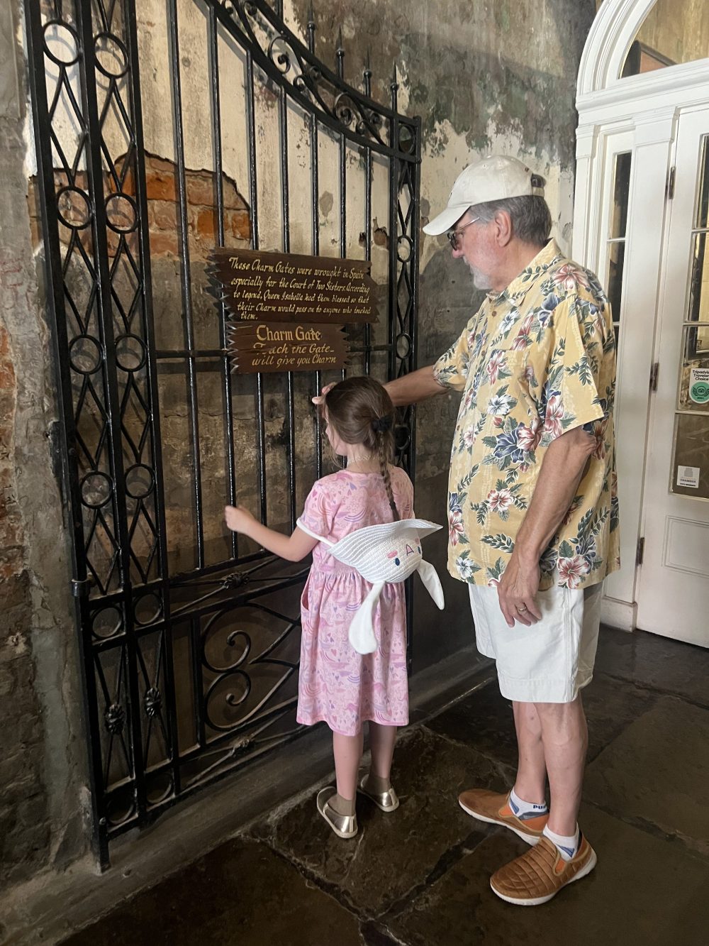 Older man and young girl reading a sign beside a historic wrought-iron gate in the French Quarter.