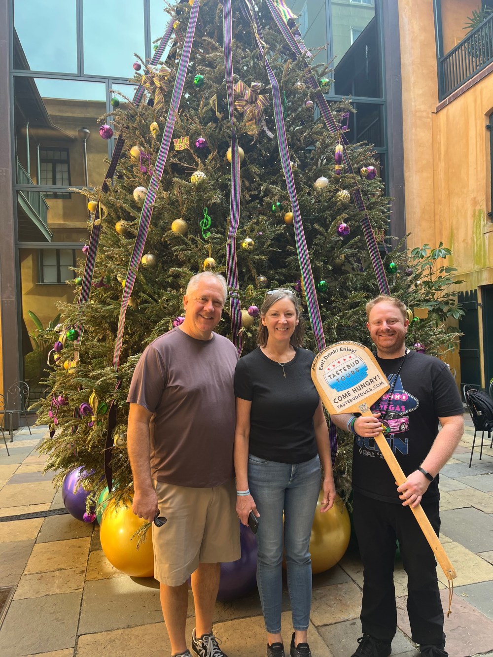 Tastebud Tours guests posing beside a decorated Christmas tree outdoors.