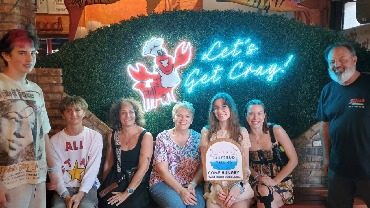 Tastebud Tours group posing inside a New Orleans restaurant beside a colorful crawfish-themed neon sign.