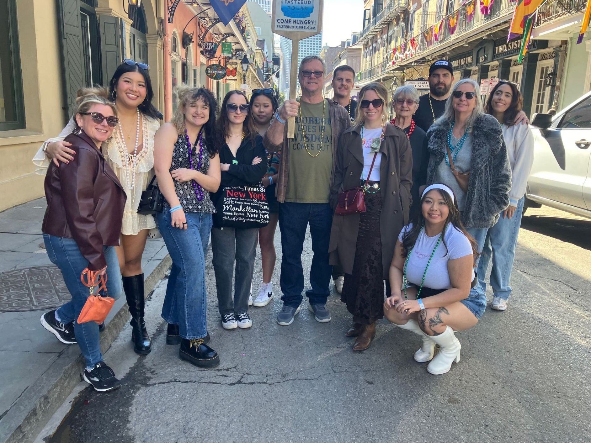 Tastebud Tours group posing on a French Quarter street decorated with colorful Mardi Gras beads.