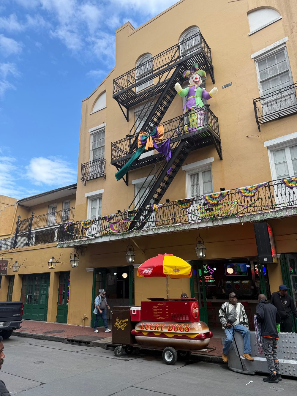 Mardi Gras decorations on a French Quarter building with a Lucky Dogs cart on the street in New Orleans.