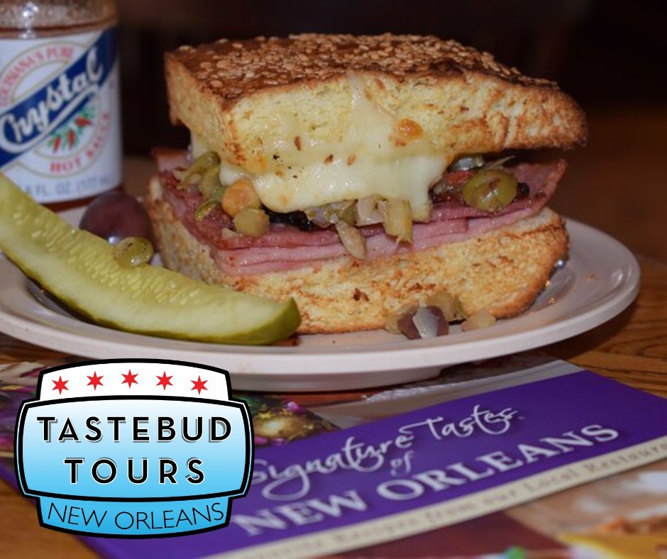 New Orleans muffuletta sandwich filled with Italian meats, melted cheese, and olive salad, served with a pickle.