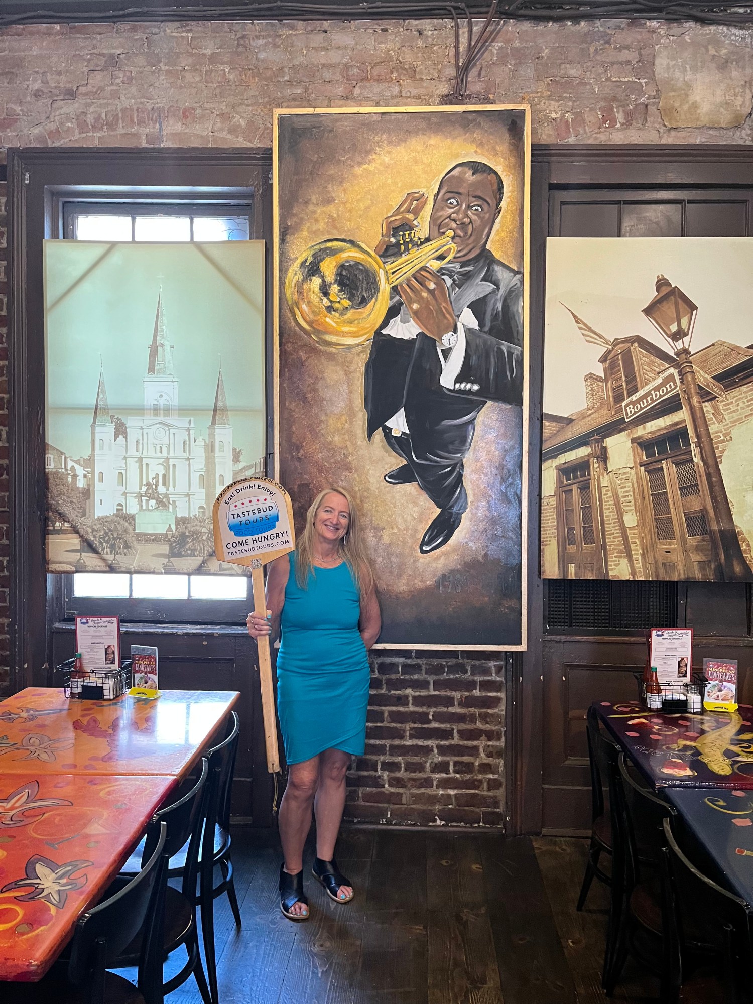 Tastebud-Tours-guide-holding-a-tour-sign-inside-a-New-Orleans-restaurant-beneath-jazz-and-Bourbon-St