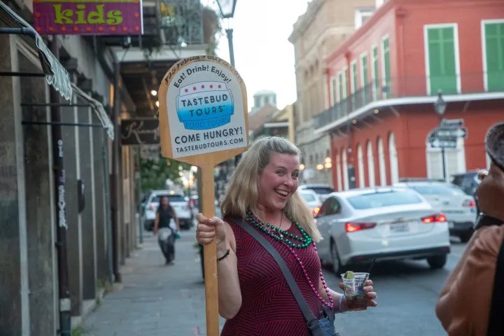 Tastebud Tours guide holding a tour sign while leading guests through the French Quarter in New Orleans.